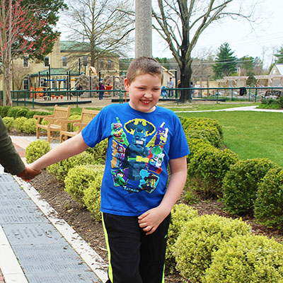 A boy in a blue shirt walks happily, holding his parents hands.