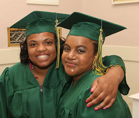Two women in green graduation gowns and caps